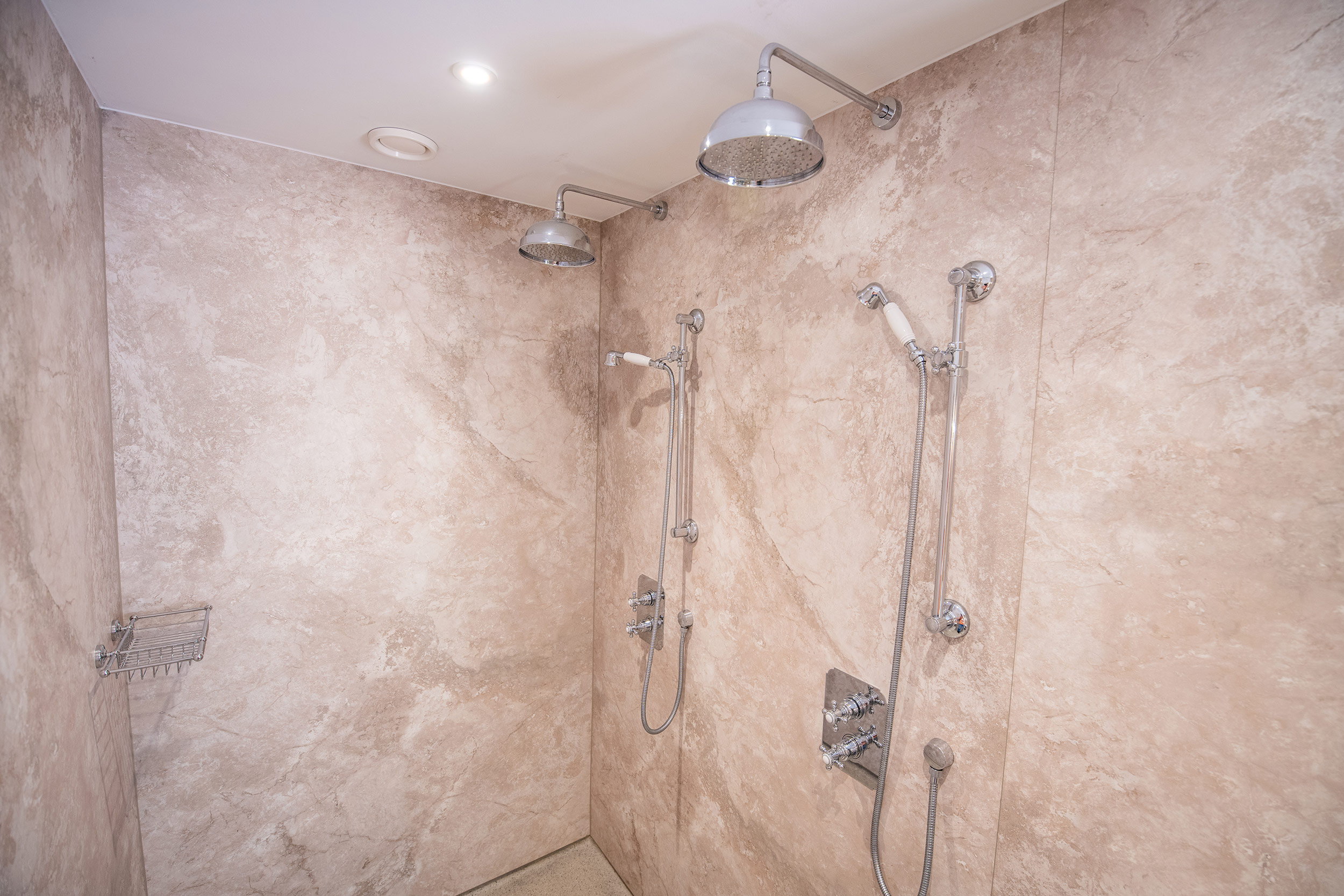 Marmerlook wandpanelen in de douches van een luxe badkamer. De voegloze wandpanelen zijn rechtstreeks over tegels geplakt met een sterke lijm.